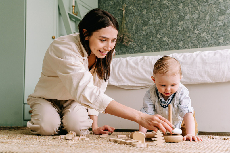 A mother and baby playing with wooden toys on the floor.