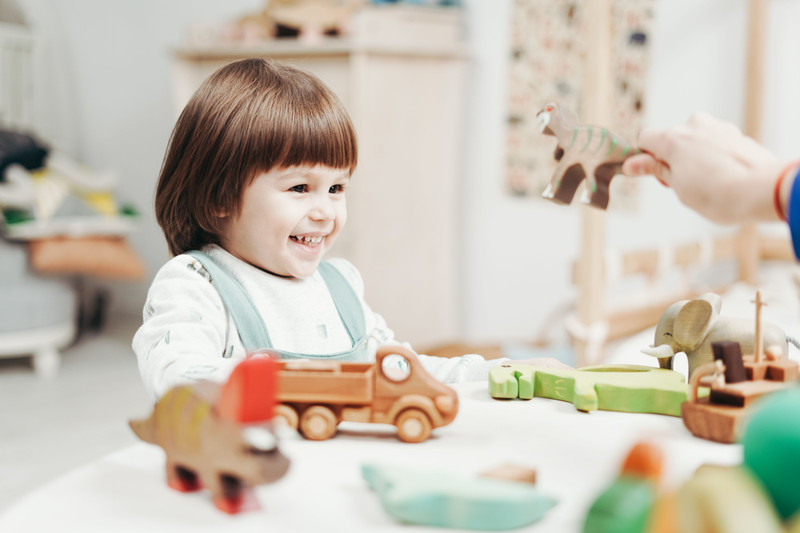 A toddler playing with a wooden car at a white table.