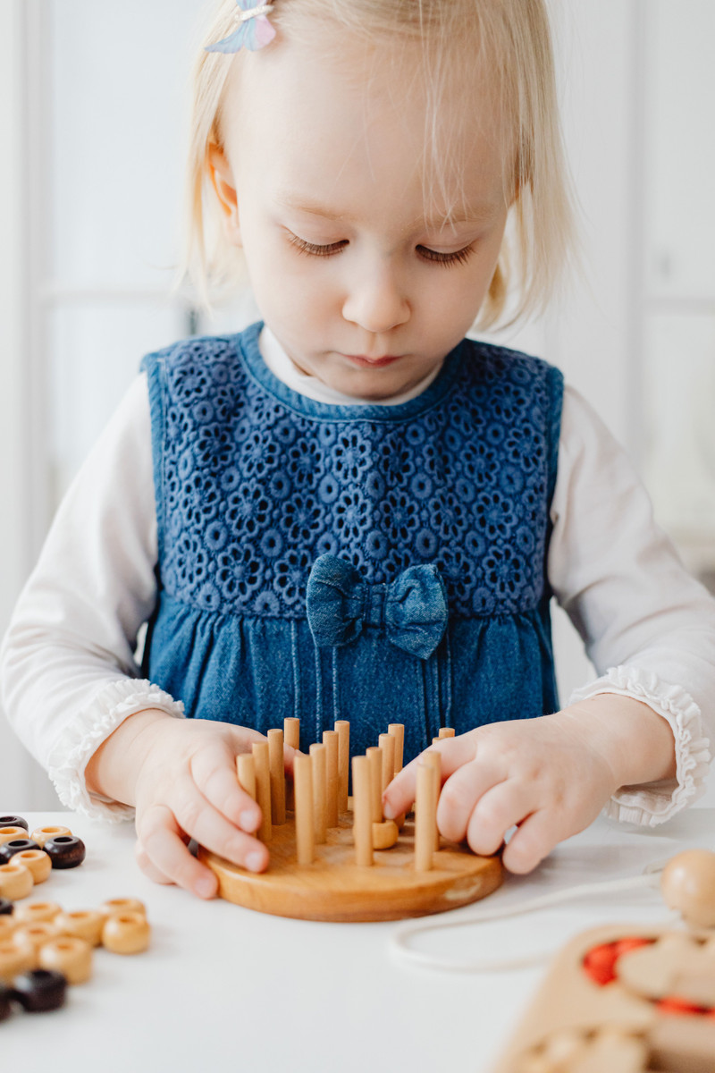 A little girl fitting wooden pegs into a puzzle.