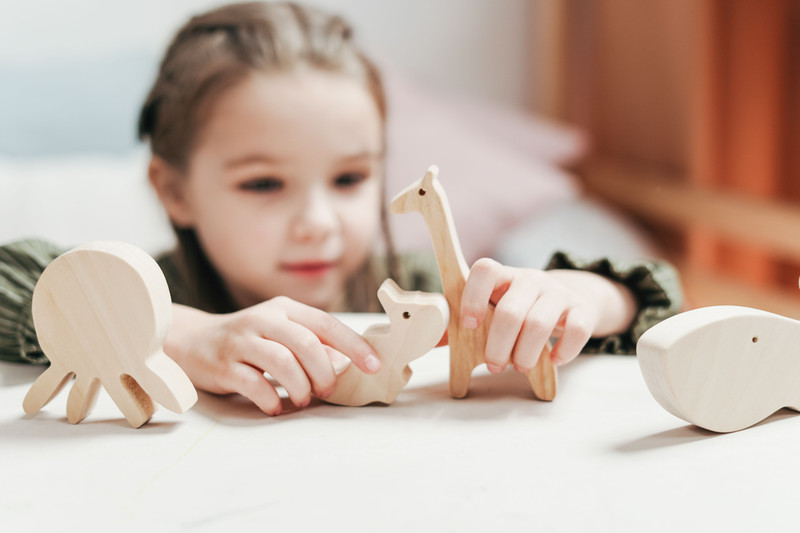 A girl lining up wooden animals on a table.
